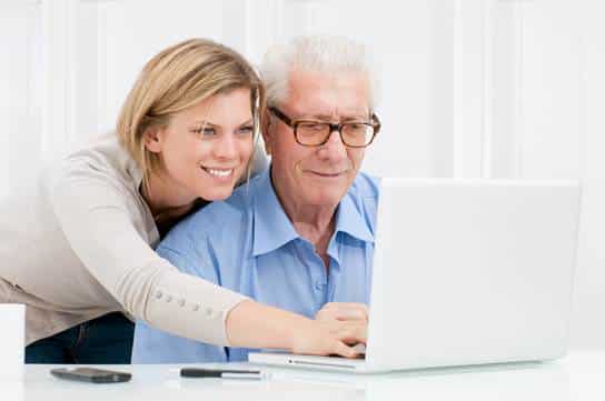 Young woman helping older man with computer