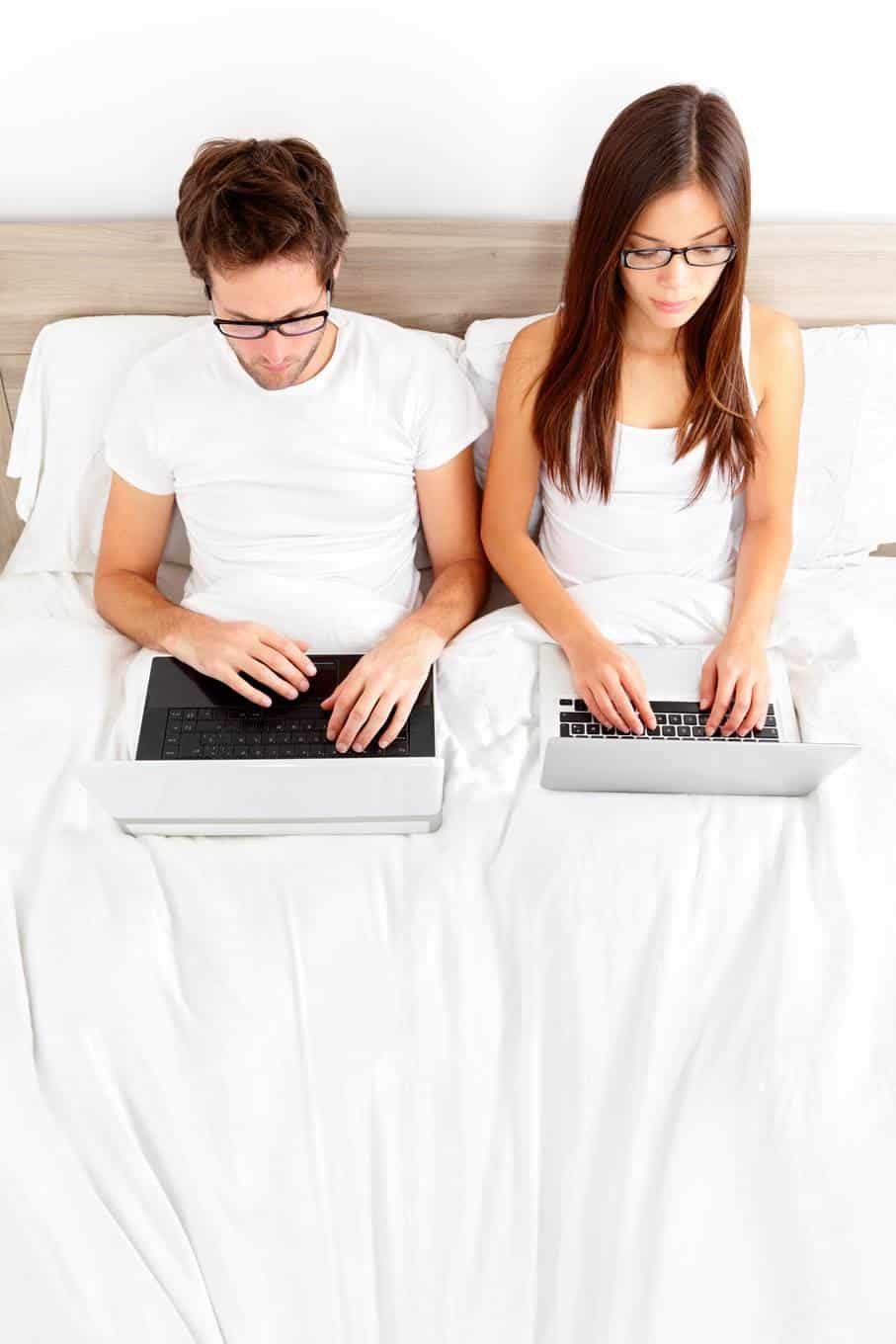 Couple sitting in bed looking at their laptops